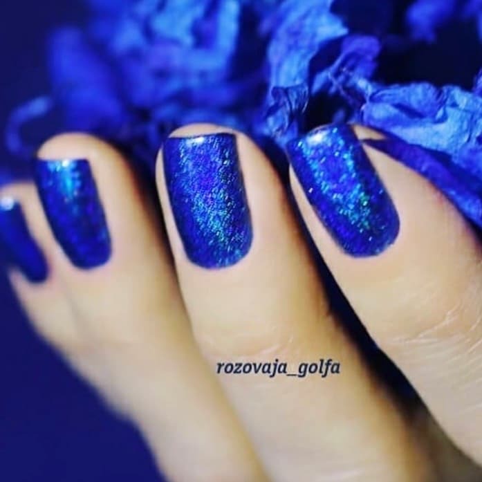 sapphire blue linear holographic nail polish by superchic lacquer shown worn on womans hands 